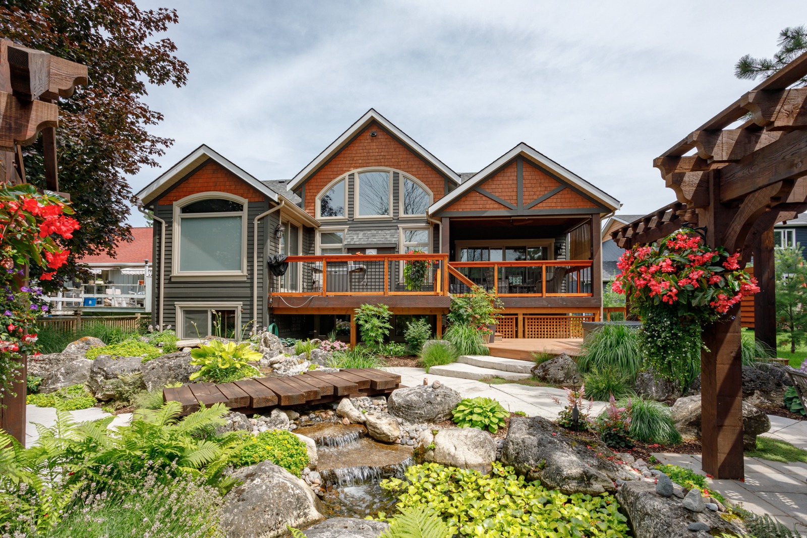 Landscaped backyard with deck, pergola, and stream