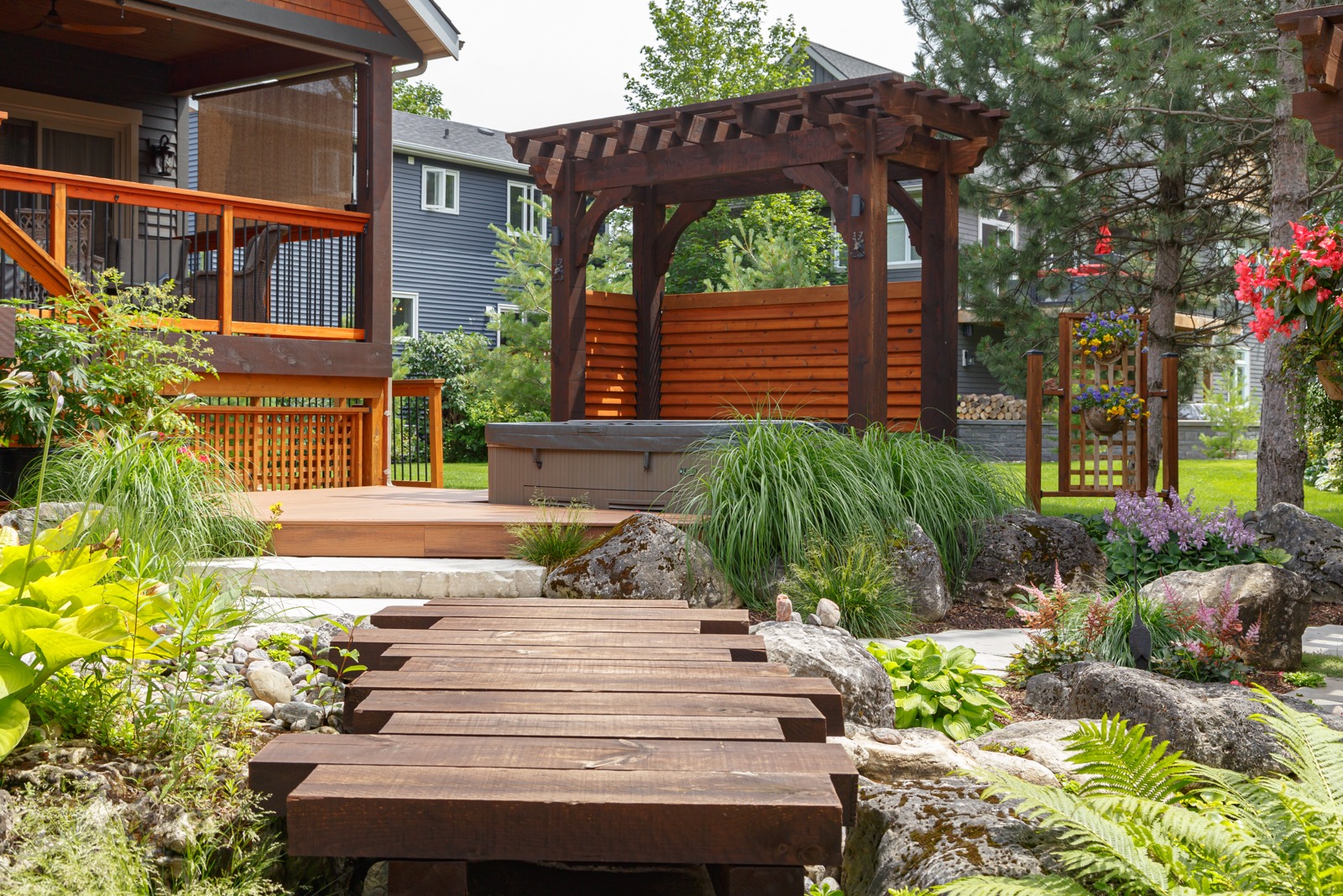 Landscaped backyard with pergola, deck, and wooden bridge