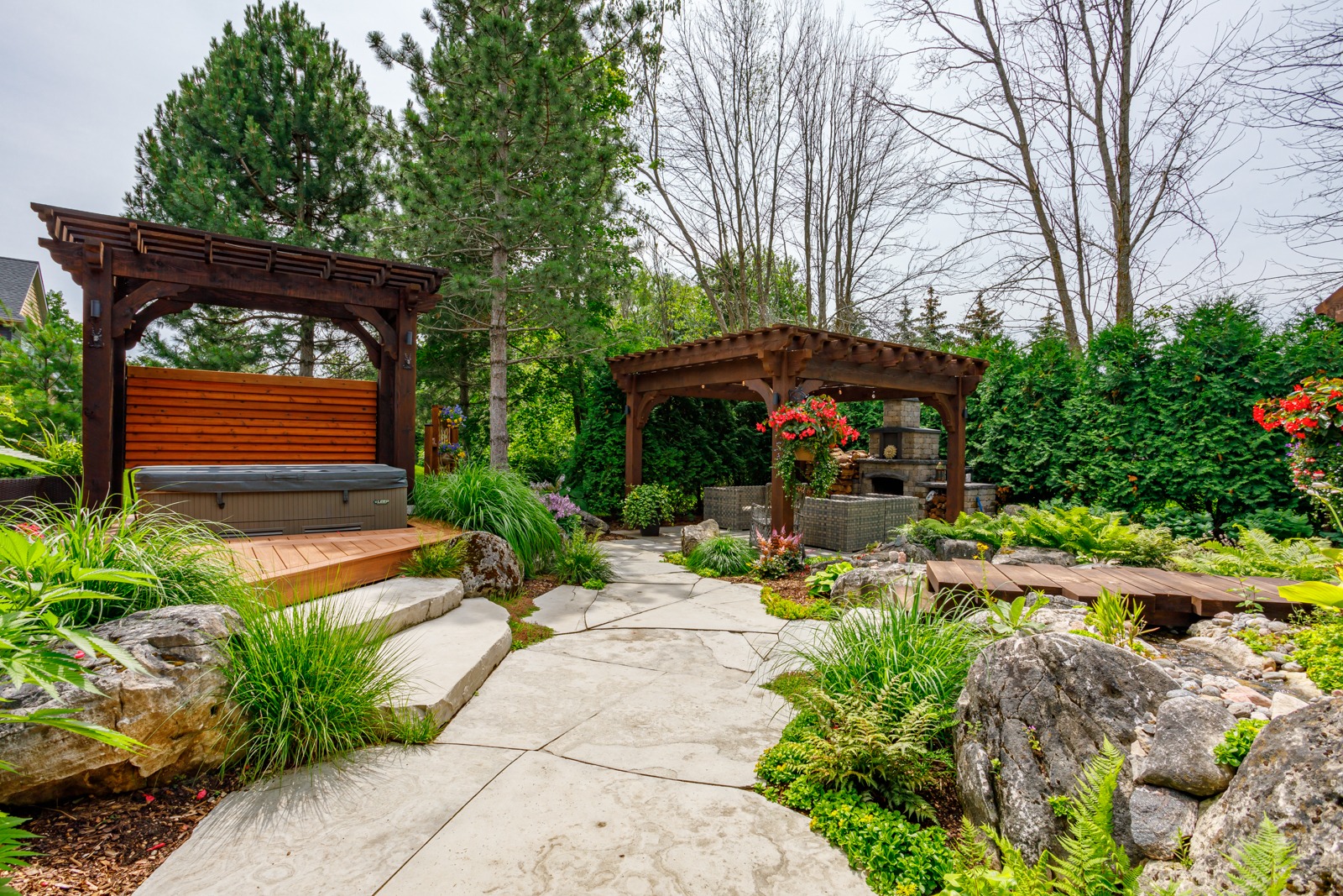 Landscaped backyard with pergolas, hot tub, and fireplace