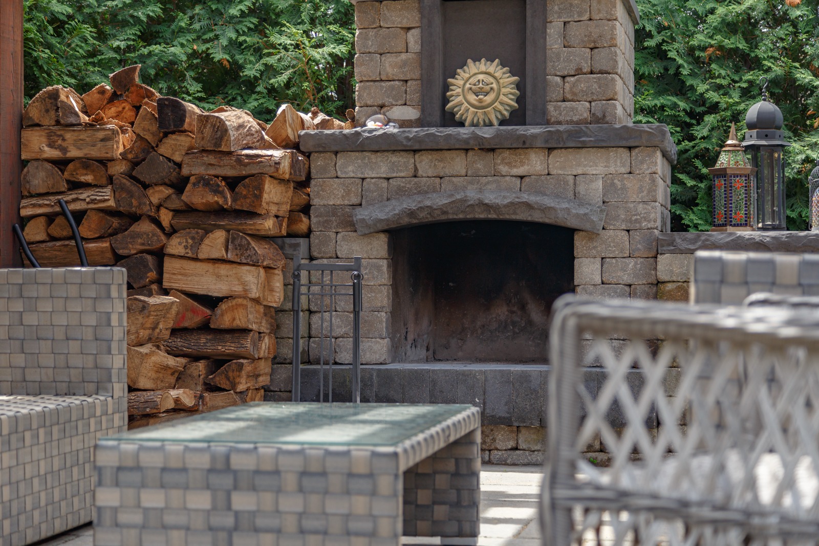 Outdoor stone fireplace with stacked firewood and patio furniture