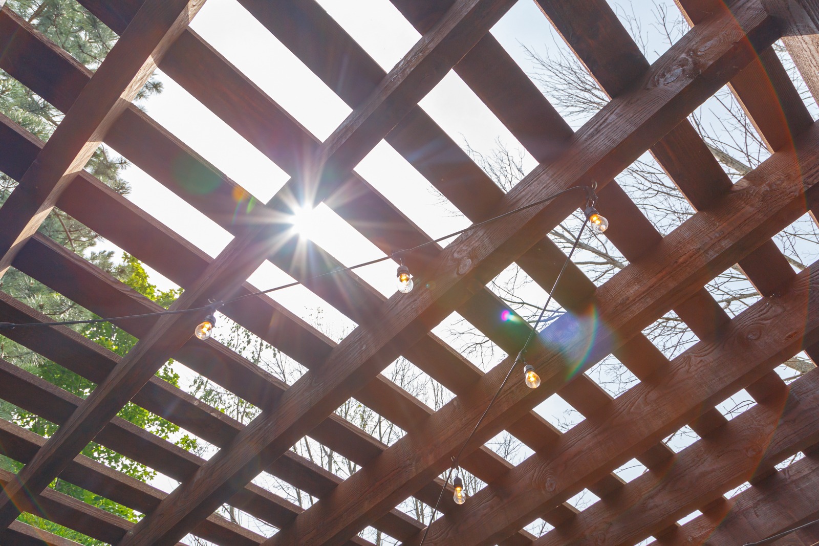 Sunlight through wooden pergola with string lights