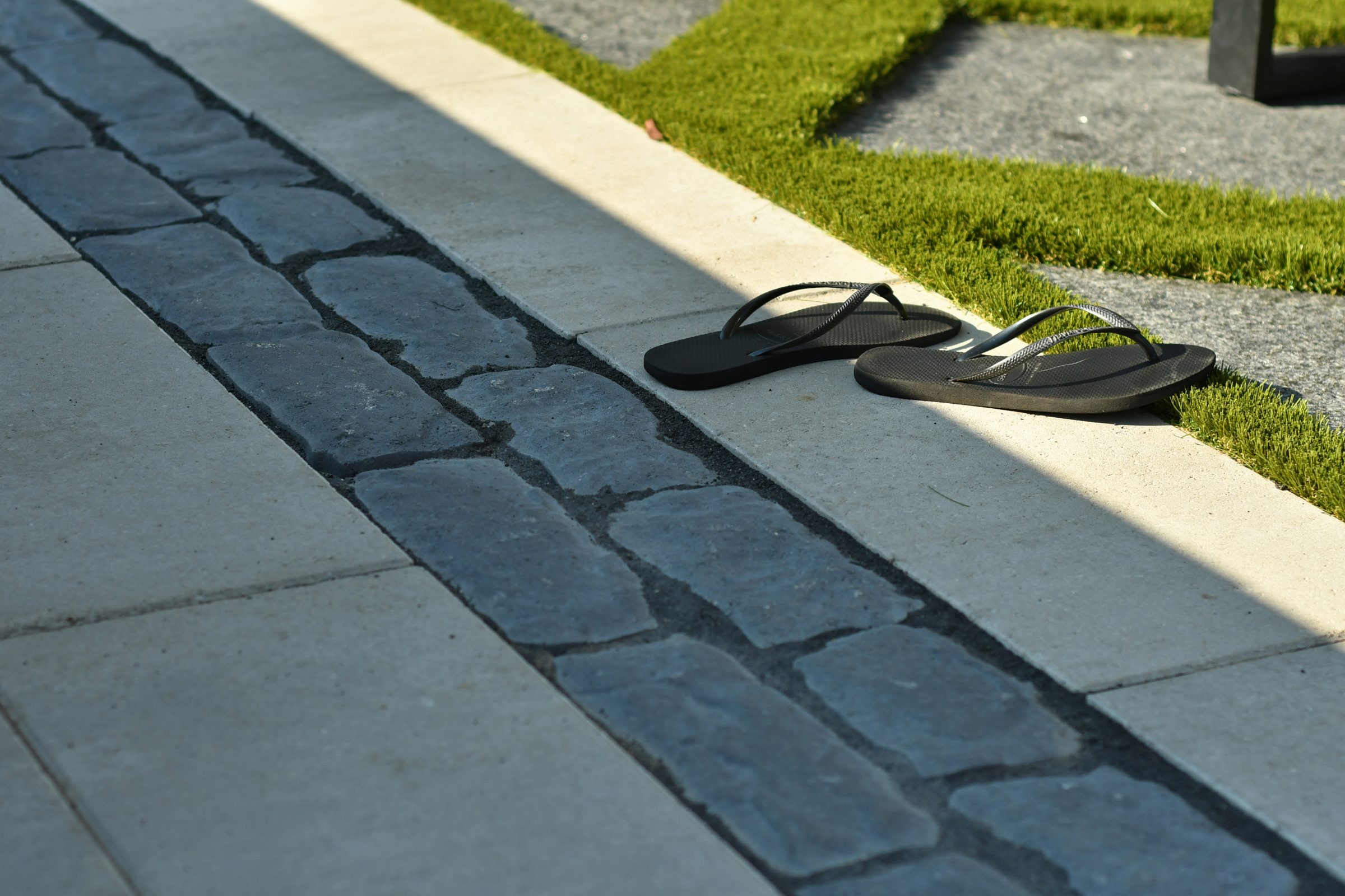 Black flip-flops on stone walkway beside grass