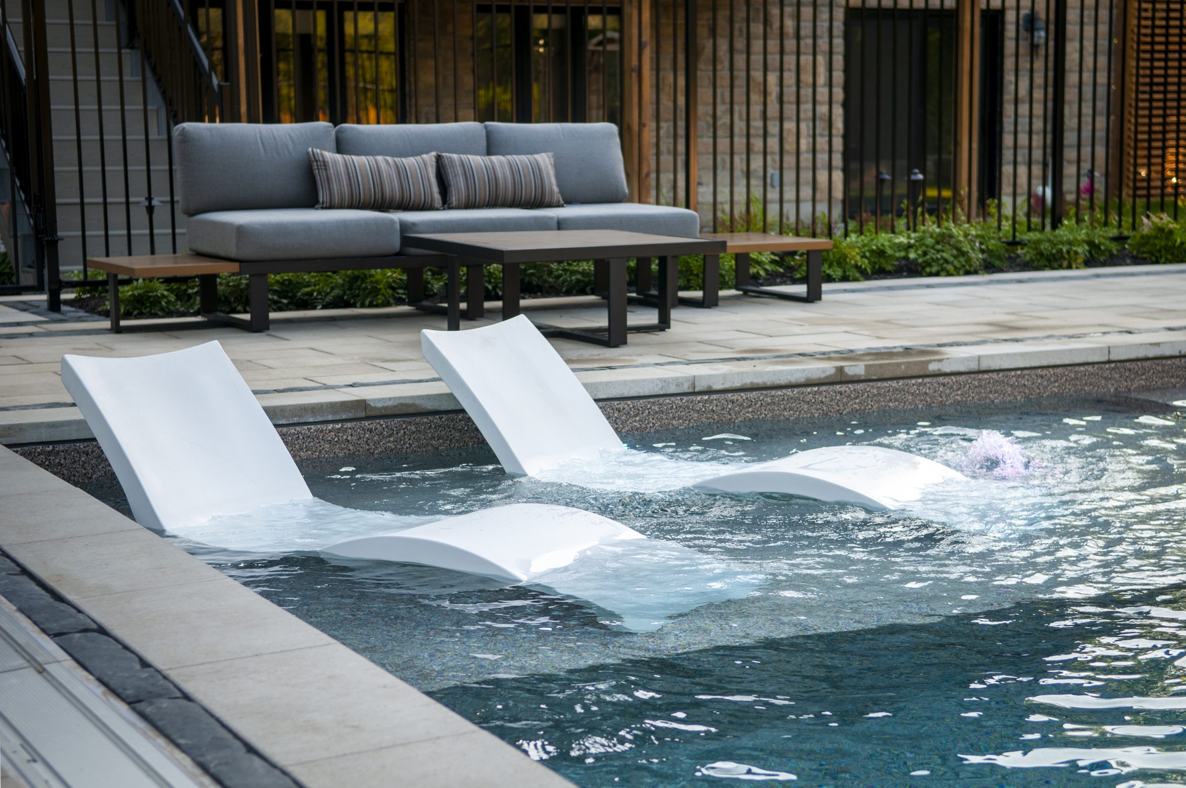 Modern pool with in-water lounge chairs and patio seating