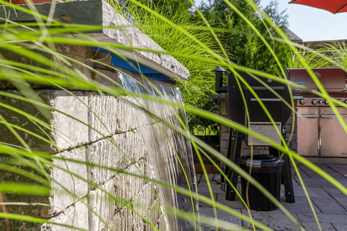 Backyard stone waterfall feature beside outdoor grill