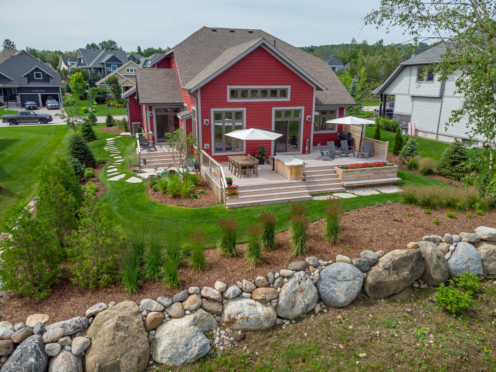 Red suburban home with landscaped backyard and deck