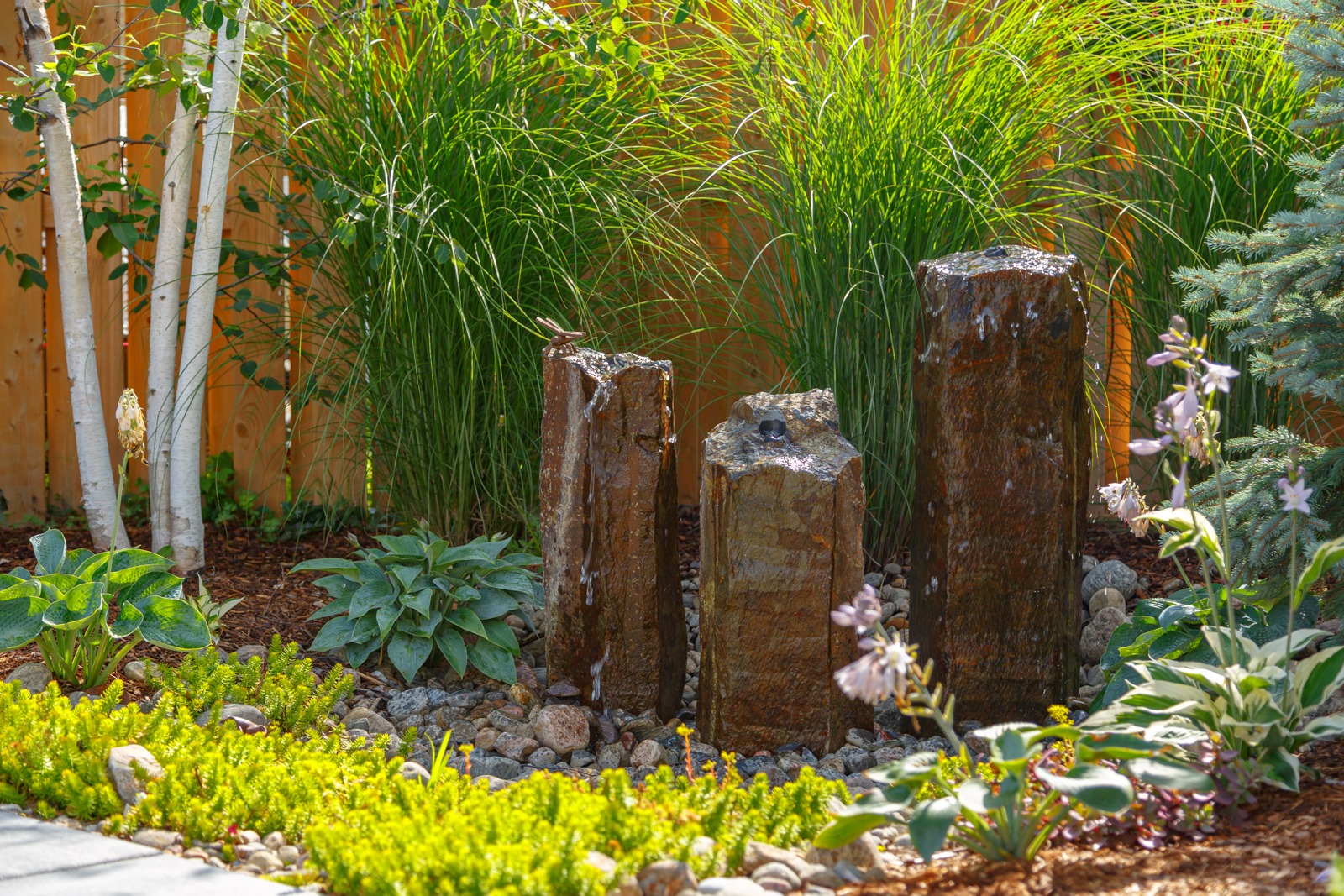 Stone pillar water fountain in landscaped backyard garden