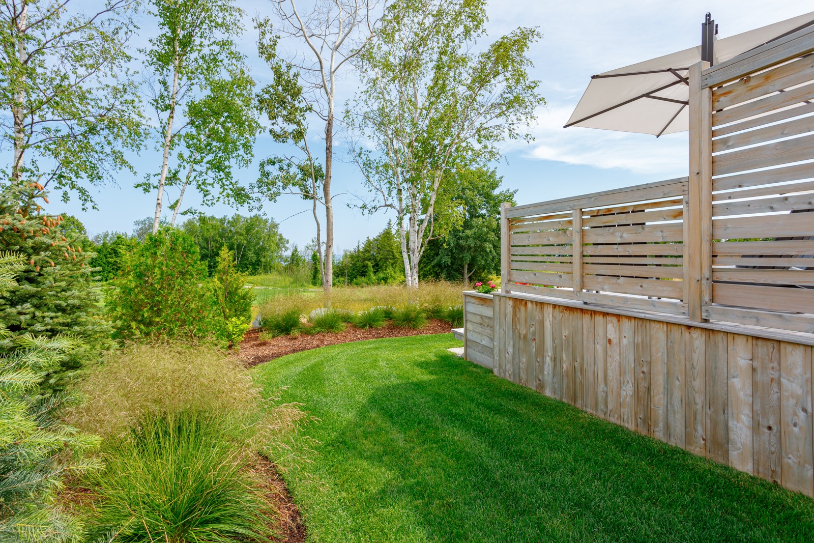 Landscaped backyard with wooden deck and privacy screen