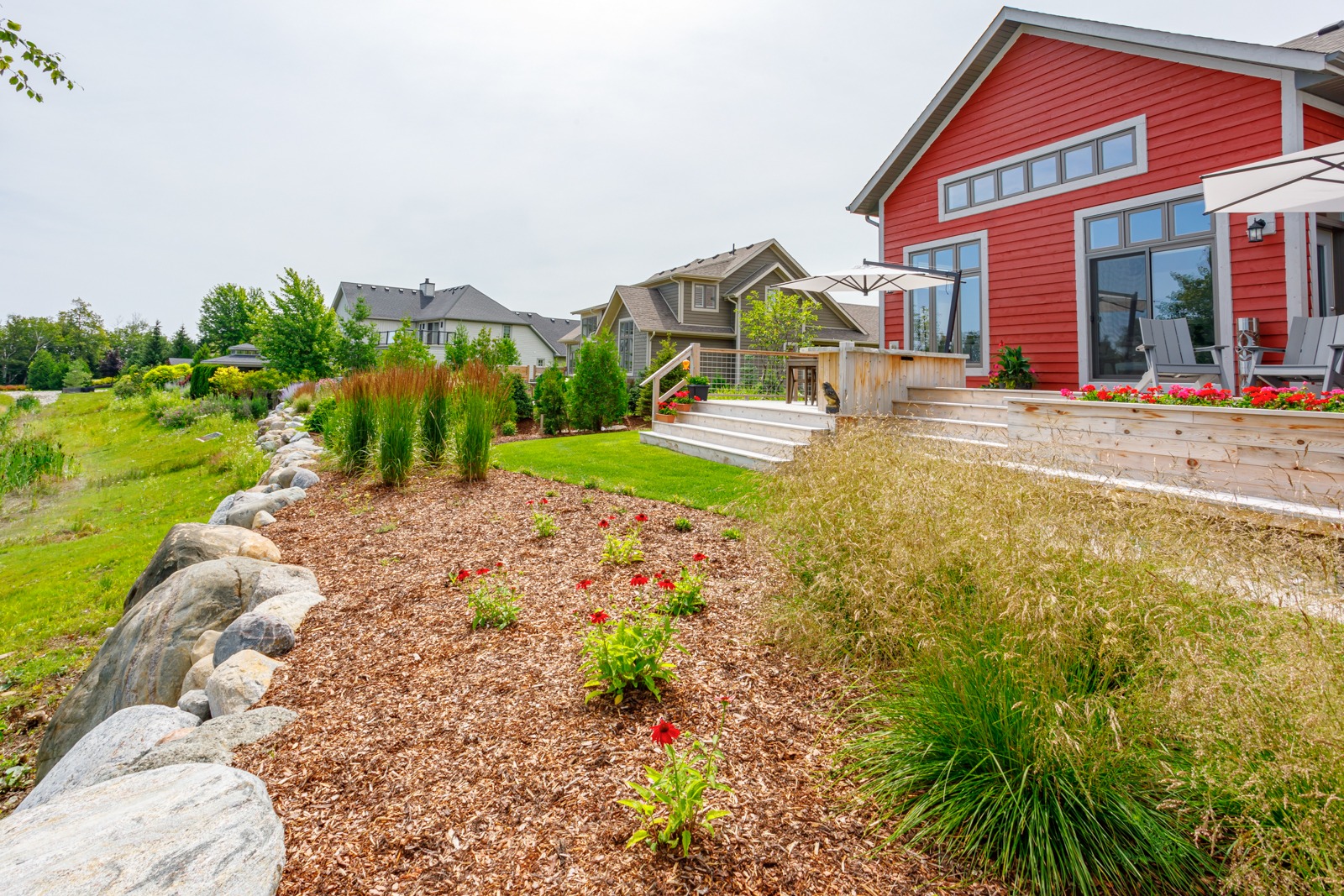 Red modern home with landscaped backyard and deck