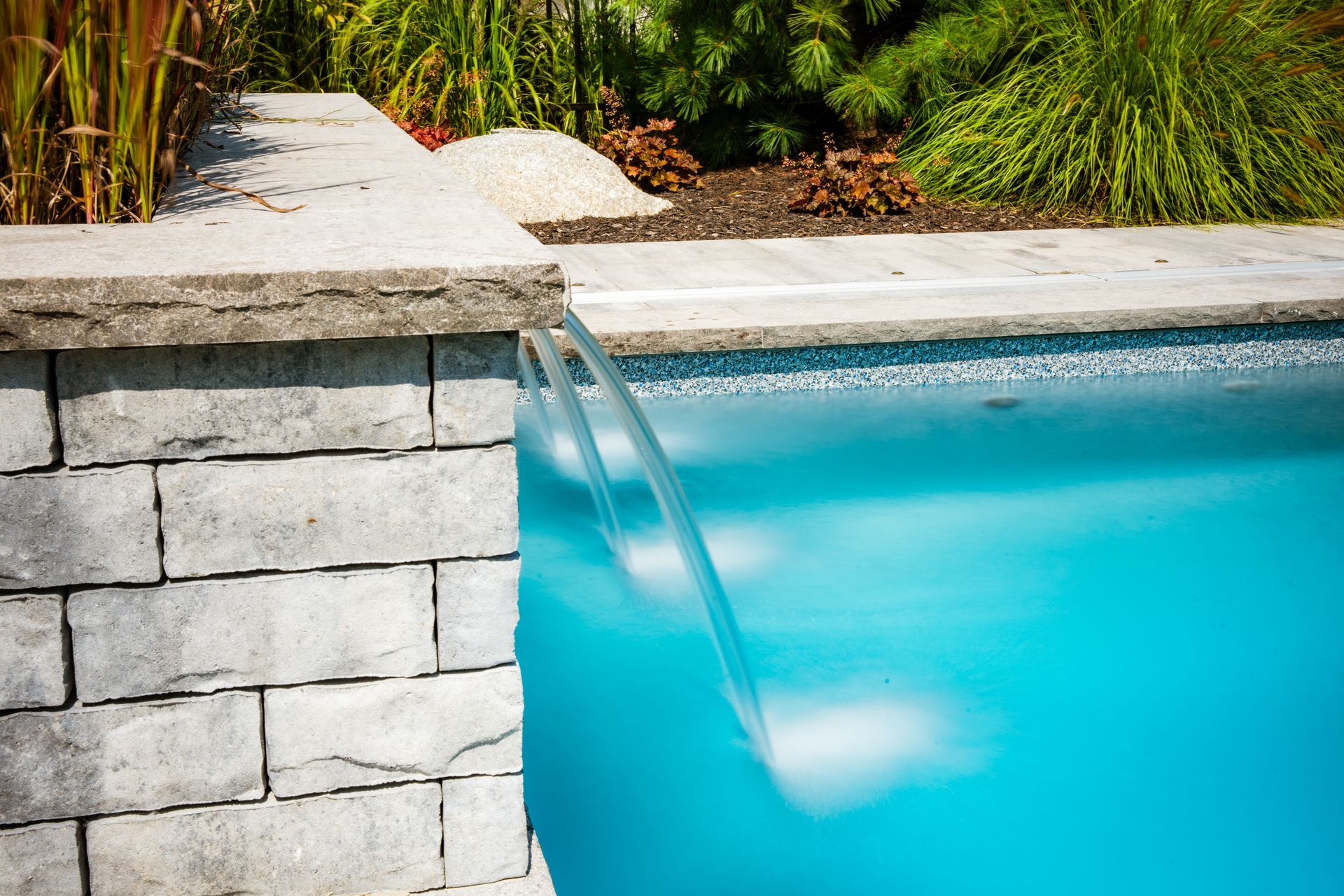 Stone waterfall feature flowing into backyard swimming pool