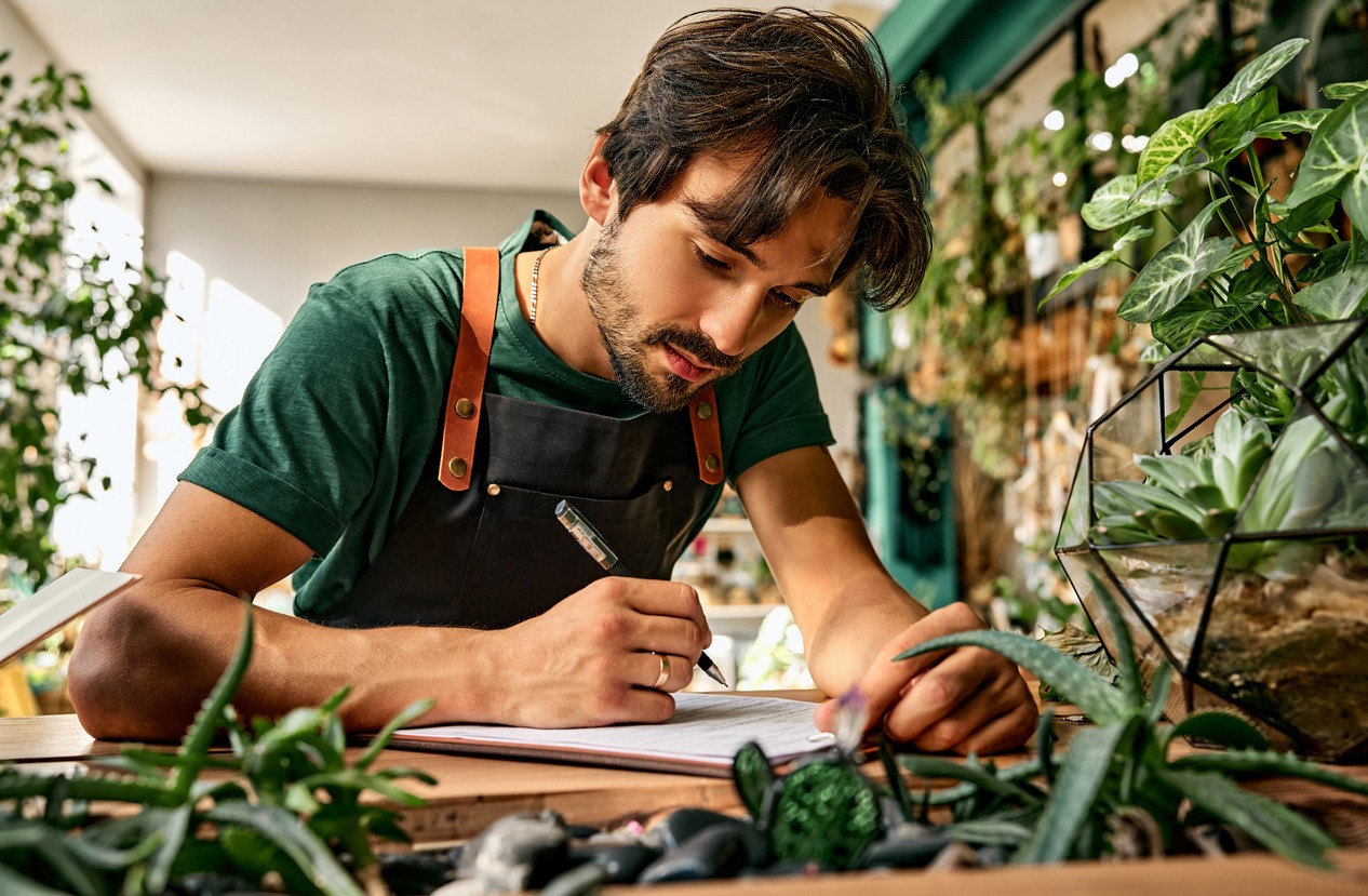 Man writing in notebook among indoor plants