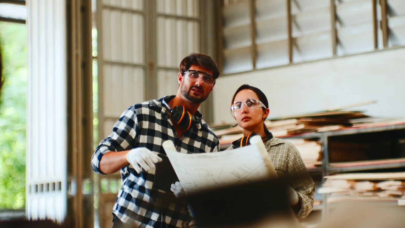 Two workers reviewing blueprints in workshop