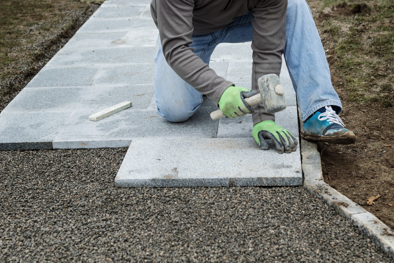 Worker installing concrete pavers with rubber mallet