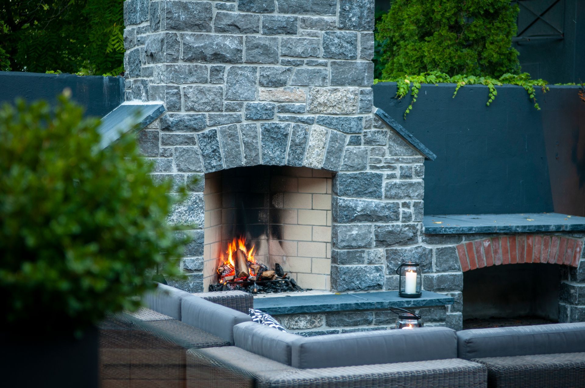 Outdoor stone fireplace with burning fire and patio seating